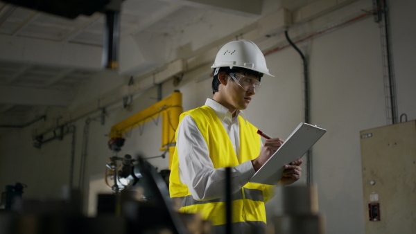 A young industrial Japanese man engineer with check list making control indoors in metal workshop