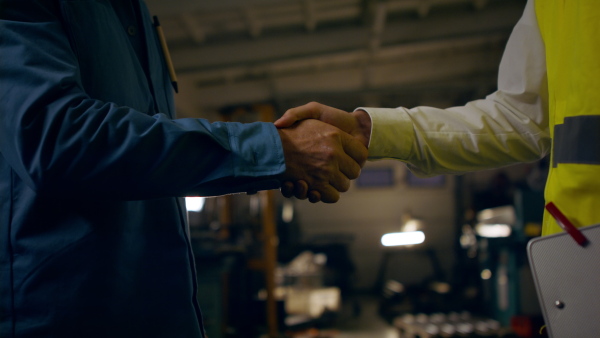 A japanese engineer shaking hands with mature wroker indoors in metal workshop, close up