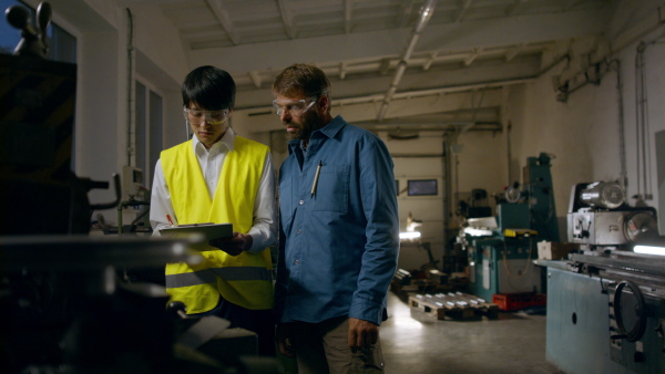 A Japanese engineer controlling mature worker indoors in metal workshop.