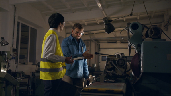 A Japanese engineer controlling mature worker indoors in metal workshop.