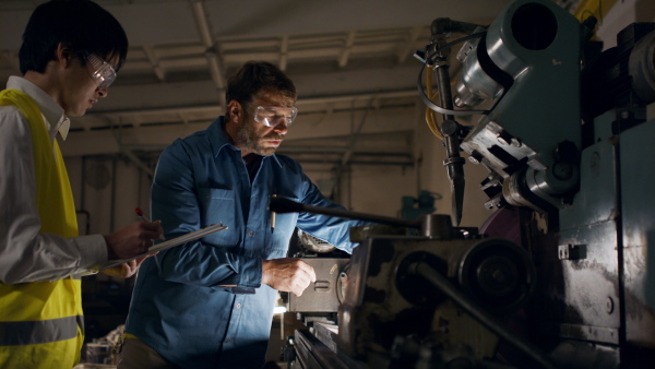 A Japanese engineer controlling mature worker indoors in metal workshop.