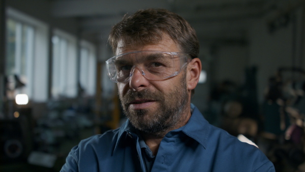 A close up of mature industrial man worker indoors in metal workshop, looking at camera.