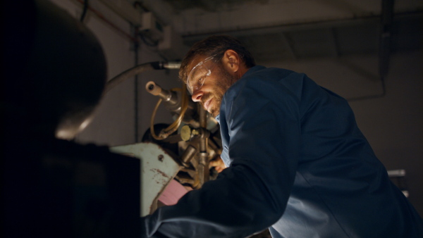 A concentrated mature industrial man working indoors in metal workshop.