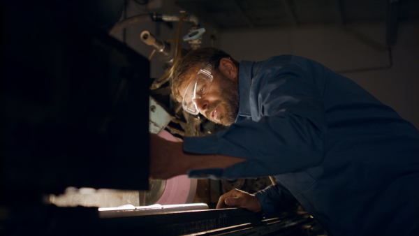 A concentrated mature industrial man working indoors in metal workshop.