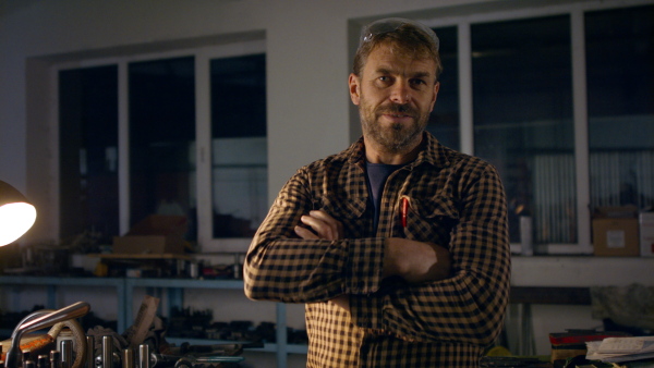 A mature industrial man working indoors in metal workshop, looking at camera.