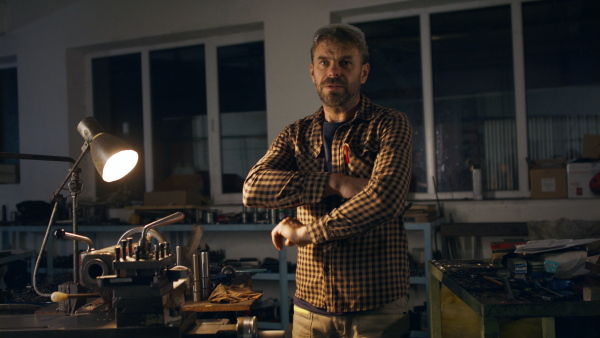 A mature industrial man working indoors in metal workshop, looking at camera.