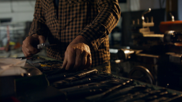 An unrecognizable mature industrial man working indoors in metal workshop, close up.