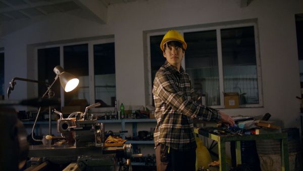 A young Japanese industrial man working indoors in metal workshop, looking at camera.