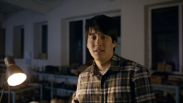 A happy Japanese industrial man working indoors in metal workshop, looking at camera.