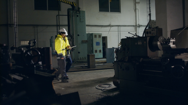 A Japanese engineer with his mature colleague talking and making control indoors in factory.