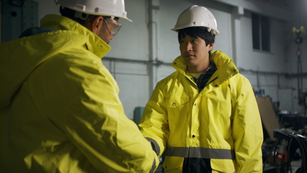 A Japanese engineer shaking hands with mature business partner indoors in metal workshop.