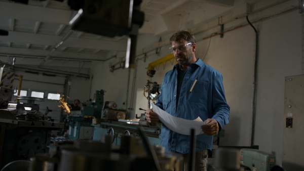 A mature industrial man working indoors in metal workshop, looking at camera.