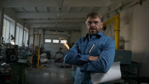 A mature industrial man working indoors in metal workshop, looking at camera.