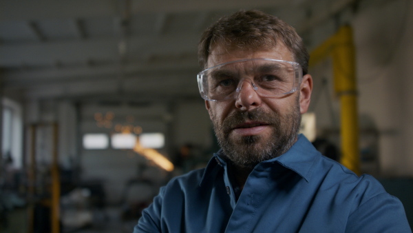 A close up of mature industrial man worker indoors in metal workshop, looking at camera.