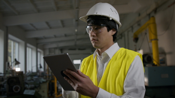 A young industrial Japanese man engineer with protective wear indoors in metal workshop.