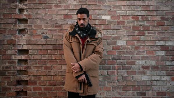 Portrait of young black man holding a gun, pointing at camera. Close up.