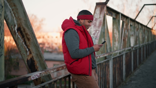 Portrait of young black man standing on old bridge, with smart phone, looking at camera, smiling.