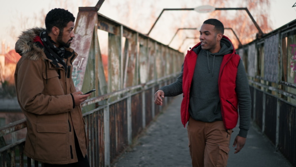 Two young friends, meeting outdoors on old bridge, greeting, smiling.