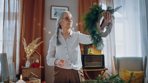 Senior woman a making Christmas wreath from natural materials indoors at home