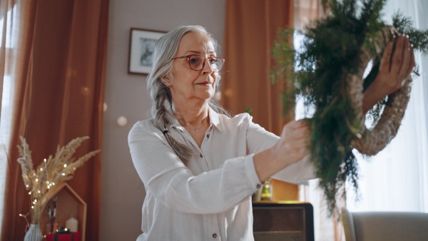 Senior woman a making Christmas wreath from natural materials indoors at home