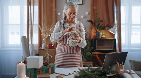 A senior woman packing Christmas present in natural eco materials indoors at home