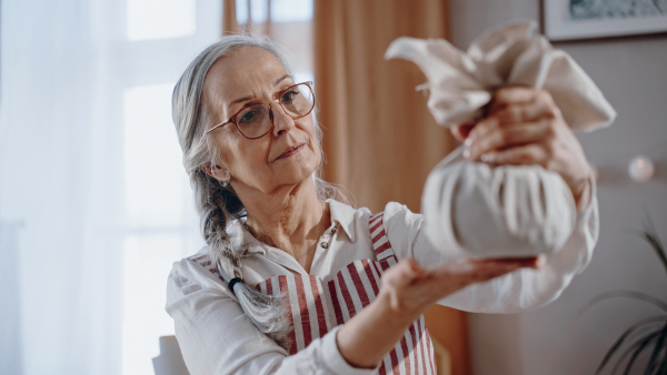 A senior woman holding Christmas present wrapped in eco materials indoors at home.