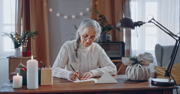 A happy senior woman writing Christmas cards indoors at home