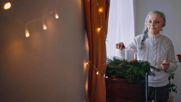 A senior woman lighting up candle at Christmas wreath indoors at home.