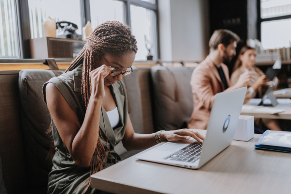 Beautiful businesswoman working on laptop in modern office. Group of freelancers working in shared work area. Concept of coworking, common workspaces for business, startups. Working remotely from coffee shop.