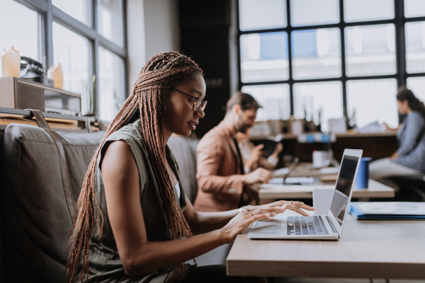 Beautiful businesswoman working on laptop in modern office. Group of freelancers working in shared work area. Concept of coworking, common workspaces for business, startups. Working remotely from coffee shop.