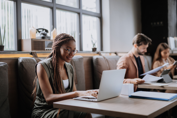 Beautiful businesswoman working on laptop in modern office. Group of freelancers working in shared work area. Concept of coworking, common workspaces for business, startups. Working remotely from coffee shop.