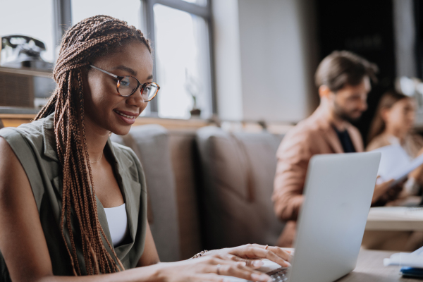 Beautiful businesswoman working on laptop in modern office. Group of freelancers working in shared work area. Concept of coworking, common workspaces for business, startups. Working remotely from coffee shop.