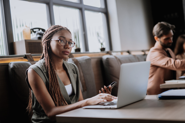 Beautiful businesswoman working on laptop in modern office. Group of freelancers working in shared work area. Concept of coworking, common workspaces for business, startups. Working remotely from coffee shop.