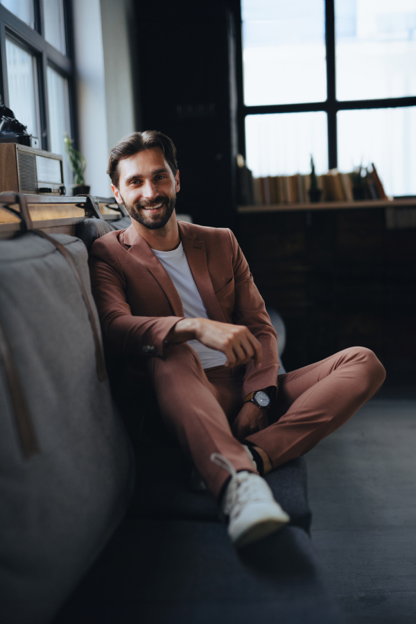 Portrait of handsome businessman in suit sitting in modern office, smiling, looking at camera. Working remotely from coffee shop.