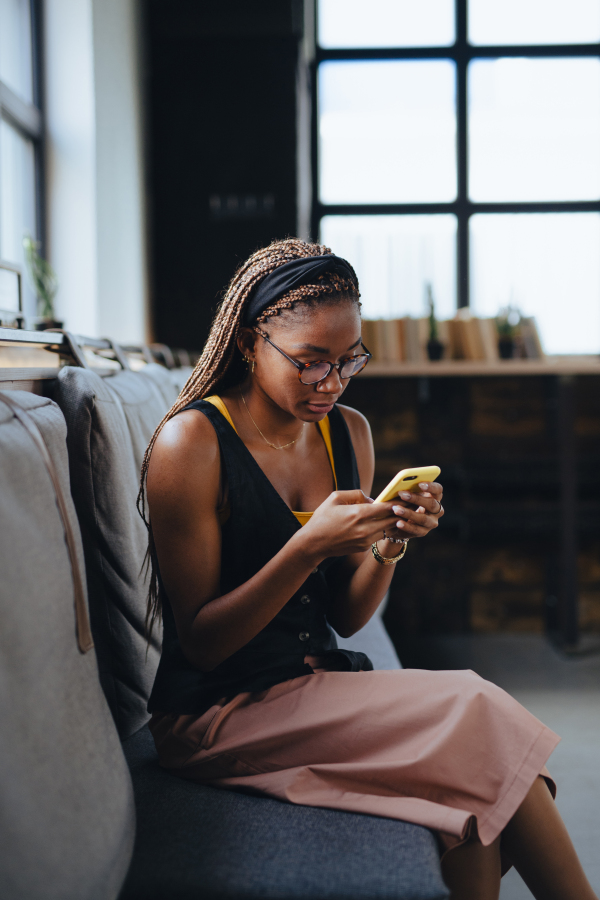 Portrait of beautiful woman sitting in modern office and looking at smartphone, taking break. Working remotely from the coffee shop, relaxed atmosphere.