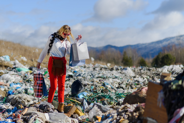 Fashionable modern woman on landfill with shopping bags, consumerism versus pollution concept.