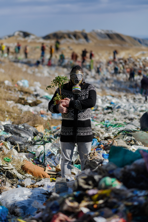 Man with gas mask holding potted plant on landfill standing on landfill, large pile of waste, environmental concept and eco activism.