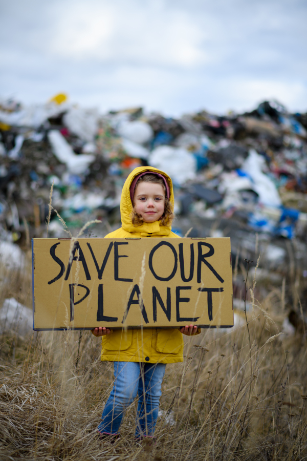 Young girl holding placard, protest sign, standing standing on landfill, large pile of waste, nature pollution environmental concept and eco activism. Greta lookalike.