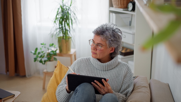 Portrait of mature woman drawing on tablet at home, looking at camera, smiling.