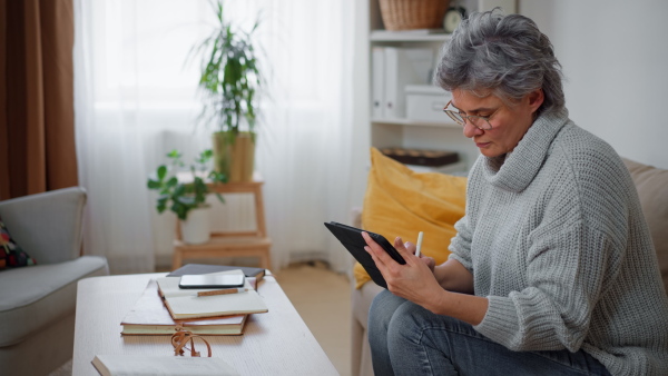 Mature woman creative drawing on tablet at home, concentrating. Camera raid.