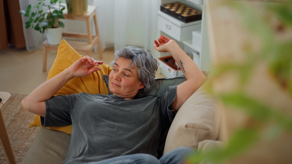 Mature grey-haired woman making herself comfortable for taking a rest on sofa at home.