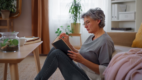 Portrait of beautiful mature woman at home, reading, drinking coffee, smiling and looking at camera.