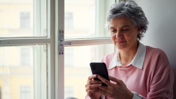 Mature woman sitting in window having video call on smart phone.