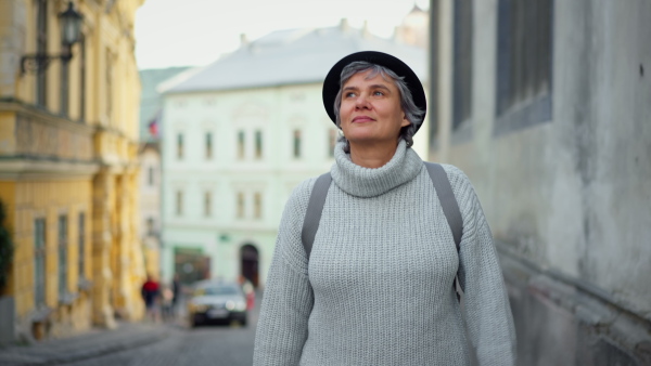 Mature woman tourist walking in historical town, smiling, enjoying.