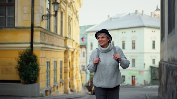 Mature woman tourist walking joyfully in historical town, smiling.