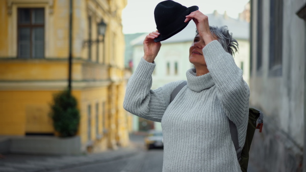 Portrait of pretty mature woman putting on hat in street and smiling into camera. Close up.