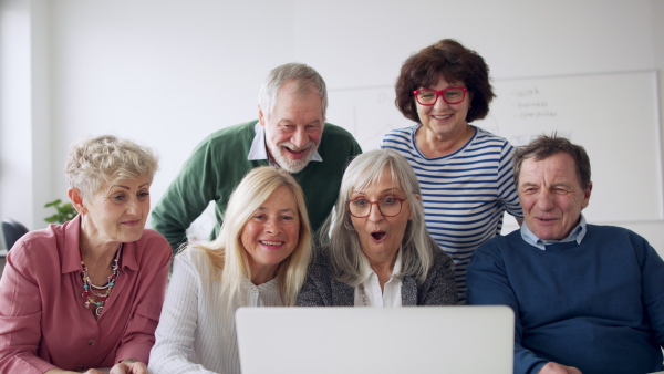 Group of cheerful seniors attending computer and technology education class, laughing and clapping.