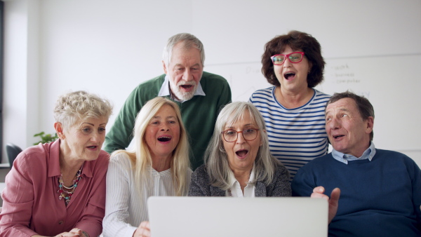 Group of cheerful seniors attending computer and technology education class, laughing and clapping.