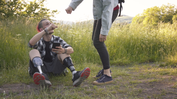 Young disabled man with leg prosthetis, sitting in nature with friend, talking.