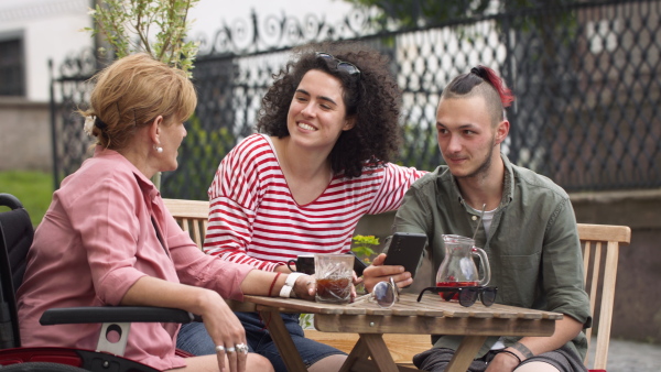 Woman on wheelchair sitting on cafe terrace with friends, talking.